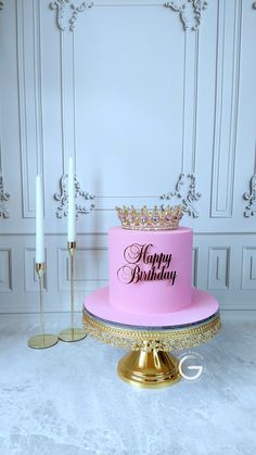 a pink birthday cake sitting on top of a gold stand next to a white wall