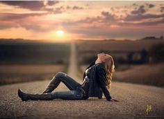 a woman sitting on the side of a road at sunset