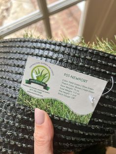 a person holding up a business card with grass growing on it in front of a window