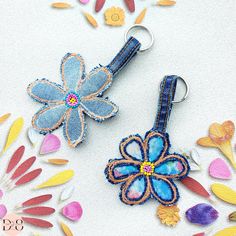 two flower shaped key chains sitting on top of a white cloth covered surface with colorful flowers