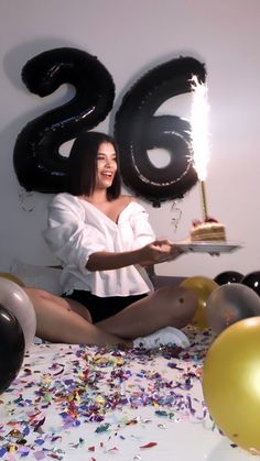 a woman is sitting on the floor with balloons and confetti in front of her