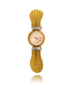 This lady's Swiss made Omega wristwatch is crafted in 18K yellow gold and has a 15mm case diameter. It displays a round shaped champagne colour dial and gold stick hour markers and hands with a crown on the back of the case. The Omega logo is at the 12 o'clock and it carries a manual winding movement. The watch is attached to an 18K yellow gold tapered loose mesh link bracelet with a fold-over clasp. Two 18K white gold bow shaped designs are attached to the band as they frame the dial and they a Yellow Gold Diamond Watch With Metal Dial For Formal, Gold Evening Watch With Jubilee Bracelet, Yellow Gold Diamond Watch With Jubilee Bracelet, Gold Diamond Watch With Metal Dial For Evening, Gold Round Diamond Watch For Formal Occasions, Gold Diamond Watch For Evening, Evening Yellow Gold Diamond Watch, Gold Diamond Watch With Jubilee Bracelet, Formal Yellow Watches With Metal Dial