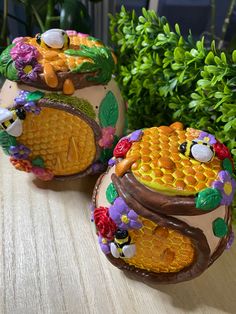 two decorated eggs sitting on top of a wooden table next to green leaves and flowers