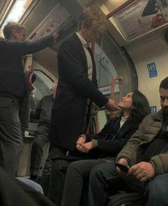 people sitting on a subway train with their hands in the air and one person standing up