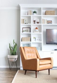 a brown leather chair sitting in front of a white book shelf with a television on top of it