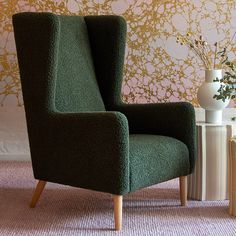 a green chair sitting next to a white vase with flowers in it on a table