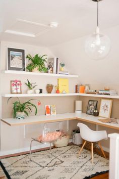 a corner desk with books and pictures on the shelves above it, along with a white chair