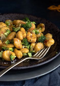 a black plate topped with broccoli and chickpeas next to a fork