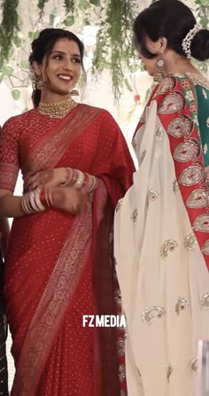 two women in red and white sari standing next to each other with their hands together