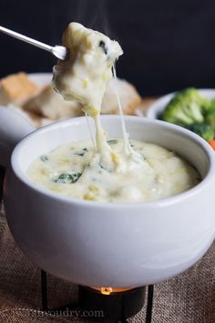 broccoli dip being poured into a white bowl with bread in the back ground