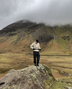 a man standing on top of a large rock in the middle of a field next to a mountain