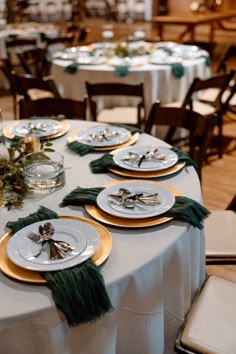 the table is set with white and gold plates, green napkins, and greenery