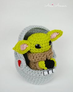 a crocheted baby yoda doll sitting in a small gray basket on a white surface