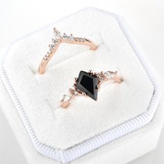 two rings sitting on top of a white cloth covered box next to each other, one black diamond and the other rose gold