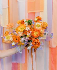 a woman holding a bouquet of flowers in front of colorful striped wallpaper with vertical stripes