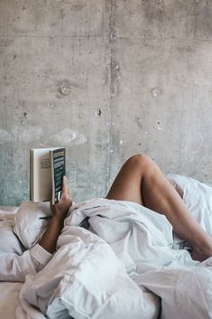 a woman laying in bed reading a book with her legs tucked under the covers,