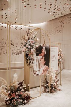 a couple kissing in front of a wedding photo frame with flowers and greenery hanging from the ceiling