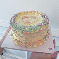 a cake with flowers and hearts on it being held by a woman's hand