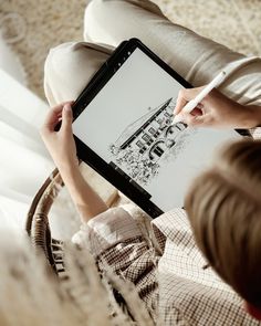 a person is drawing on a tablet with a pen in their hand while sitting on a couch