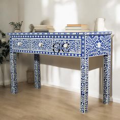 a blue and white painted table with drawers on the top, next to a potted plant