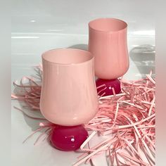 two pink vases sitting next to each other on top of some sticks and straw