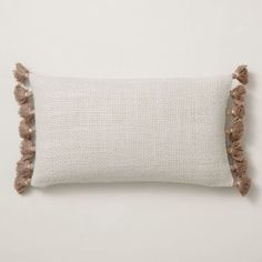 a white pillow with brown tassels on the front and back, against a white wall