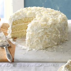 a white cake with coconut frosting on a cutting board next to a slice missing from it