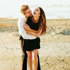 a man and woman hugging on the beach with water in the backgrouds