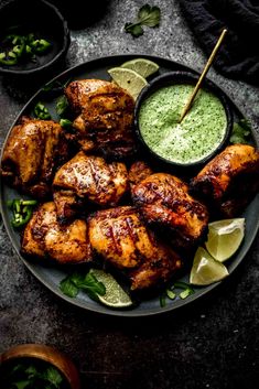 grilled chicken on a plate with green sauce and garnished with limes