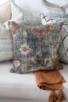 pillows and throw pillows on a couch with tassels in the foreground, along with an orange throw pillow