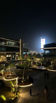 people are walking around outside at night in front of a large building with lights on it