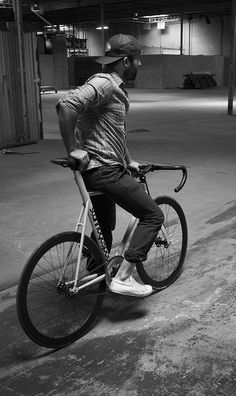 black and white photograph of man on bicycle in parking garage with no one around him