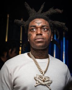 a man with dreadlocks wearing a white shirt and gold chain around his neck