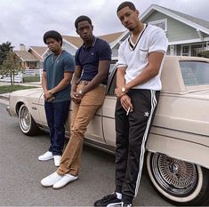 three men standing next to a car in front of a house and one is leaning on the door