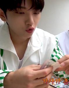 a young man wearing a green and white striped shirt is looking at his cell phone