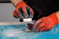 a man in red gloves and black shirt cutting something on a blue surface with scissors