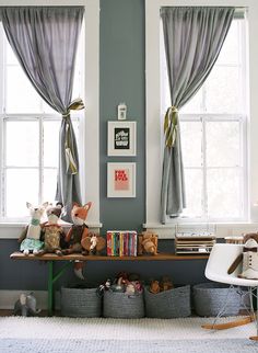 a room with two windows and stuffed animals on the shelf