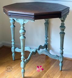 an old table is painted blue and has a pink flower on the floor next to it