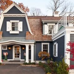 a blue house with white trim and shutters on the front door is surrounded by fall foliage