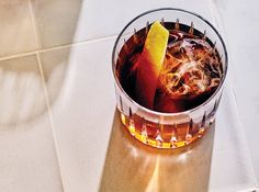 a drink in a glass with ice and a yellow leaf on the rim, sitting on a white tile floor