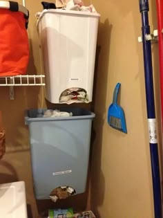 there is a trash can next to the toilet in this small room with brooms on the floor