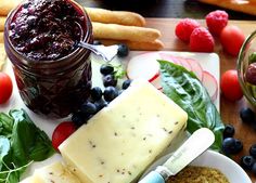 cheese, fruit and jam on a plate with breadsticks next to it in front of them