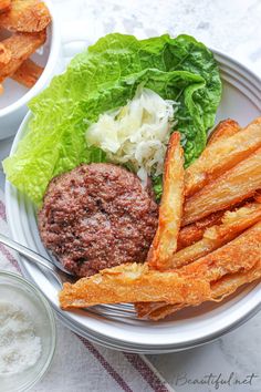 a white plate topped with lettuce and fries next to a bowl of dip