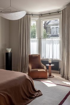 a bed room with a neatly made bed next to a chair and a large window