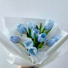 a bouquet of blue tulips is wrapped in white paper and held by someone's hand