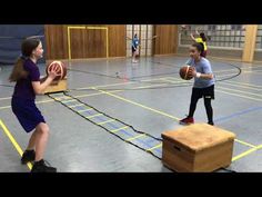 two girls are playing basketball in an indoor gym with boxes on the floor and one girl is holding a ball