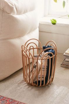 a wooden basket filled with clothes on top of a floor next to a white couch