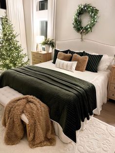 a bedroom with a large bed covered in green blankets and pillows next to a christmas tree