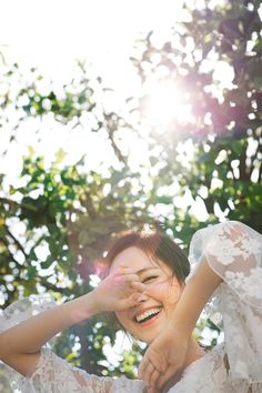 a woman in a white dress is smiling and holding her hand up to her face