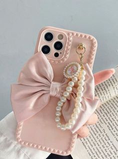 a cell phone case with pearls and a bow on the front, sitting next to an open book